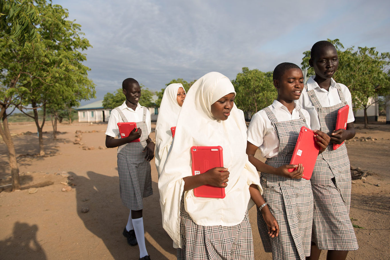Merinas Ngendayniye Mumina Khalif Mary Nyalat walk with their classmates and tablets through the school grounds