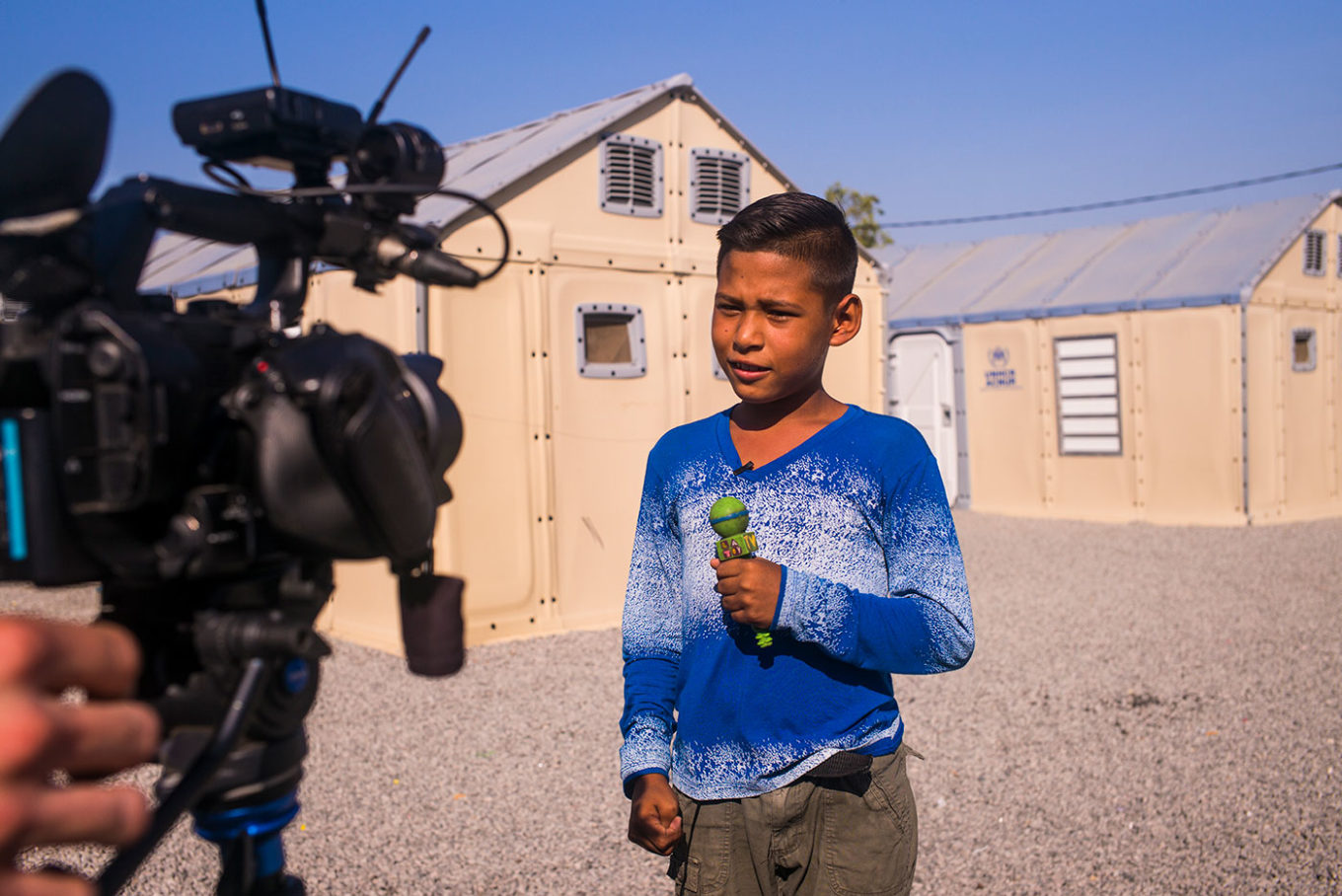 Moises (10) plays Journalist interviewing refugees in front of their shelter in Rondon 3 temporary shelter.